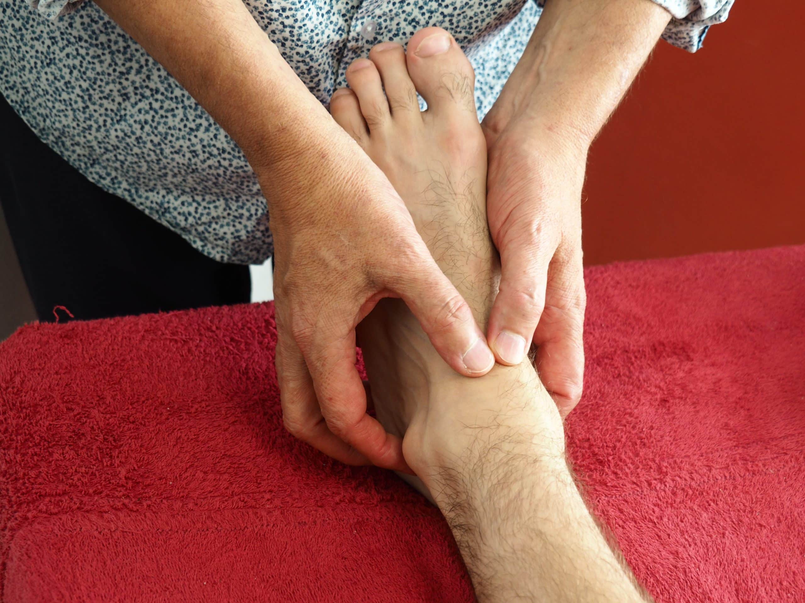 Travail sur l’astragale : les deux mains du thérapeute enveloppent le pied d’une personne allongée. Méthode Poyet.