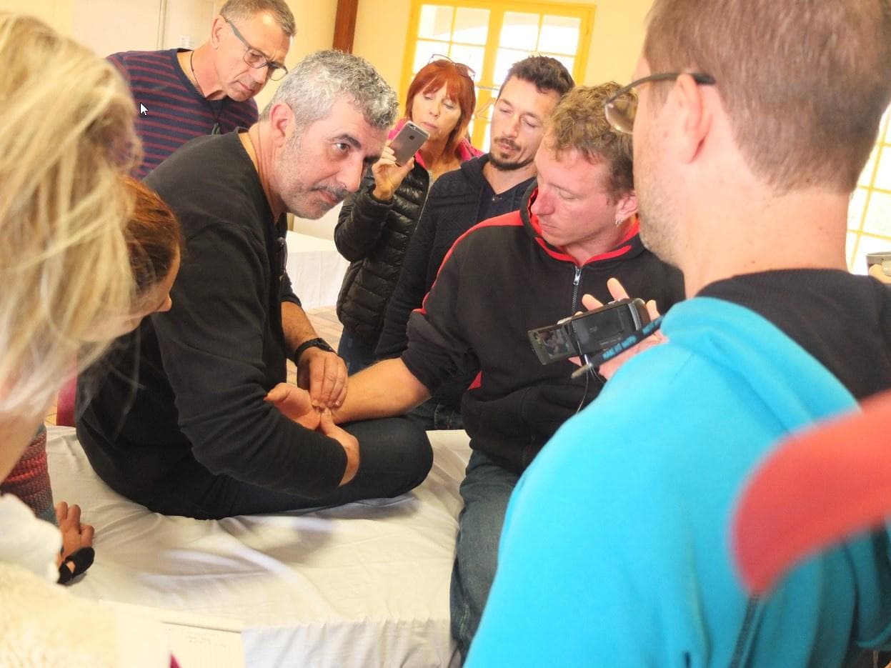 Bruno Olivié montrant une prise du poignet à un groupe d’étudiants réunis autour de la table.
